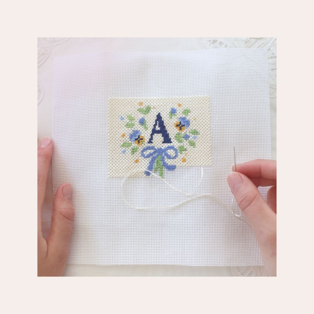 A woman is completing her Sweet Coast Monogram needlepoint project with the letter A.