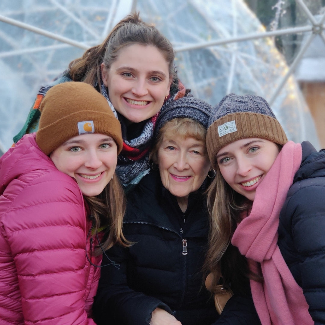 Three young women are smiling with their grandmother outside on a cold day.