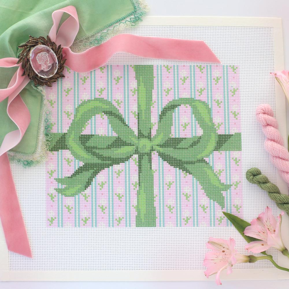 Pink Bow Needlepoint Canvas surrounded by pink and green thread and fresh flowers.
