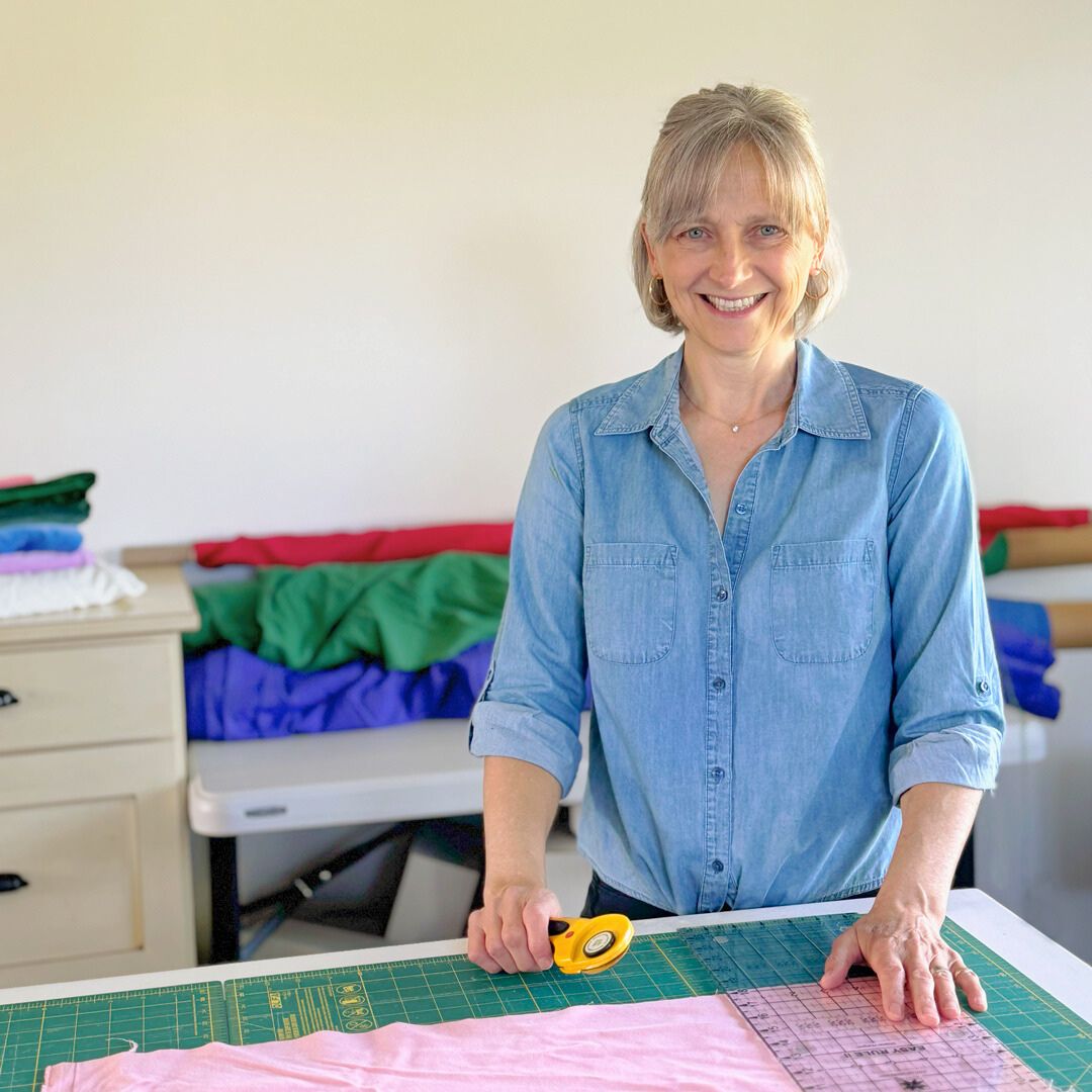 A woman with a striped button down shirt is cutting fabric on a craft table.