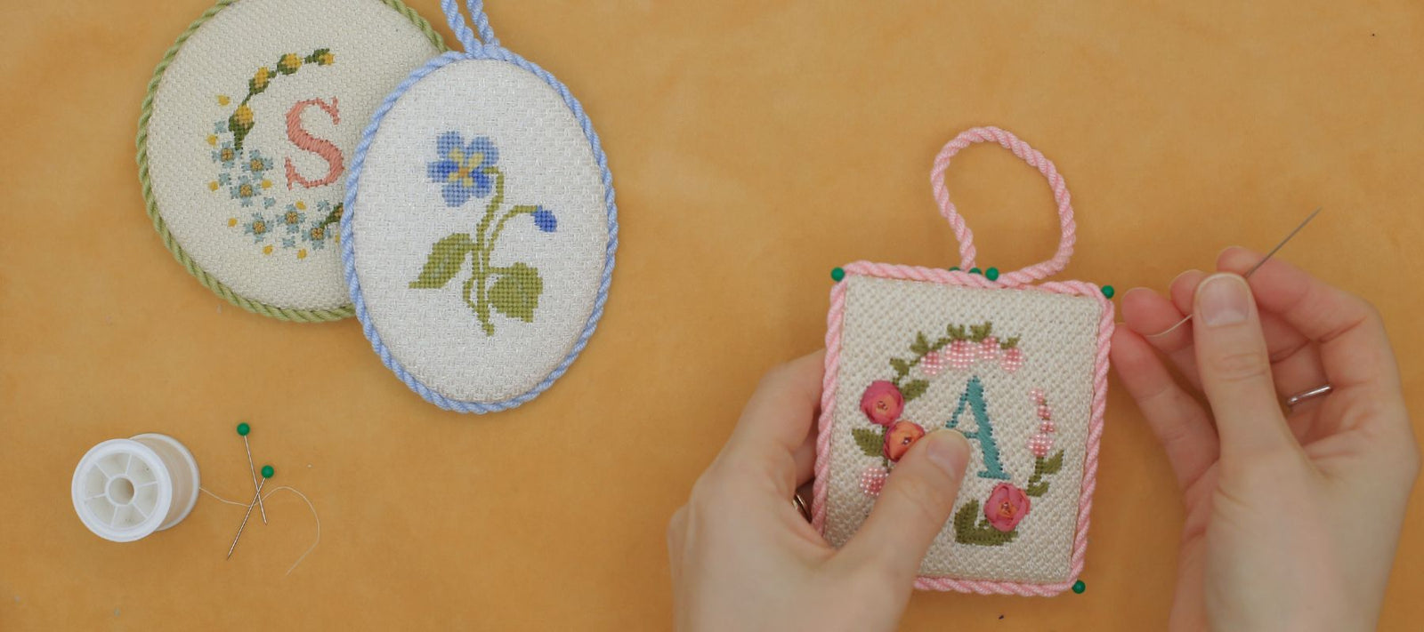 A woman is stitching a monogram needlepoint ornament.