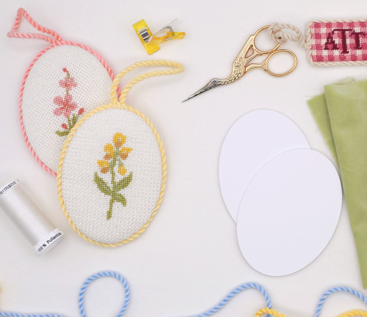 Two finished wildflower needlepoint ornaments sit next to finishing supplies.