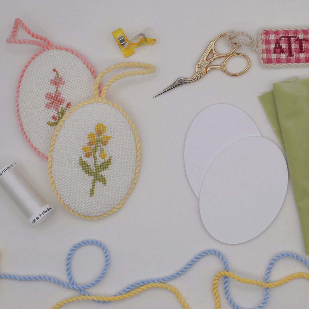 Two finished needlepoint ornaments lay next to finishing supplies.