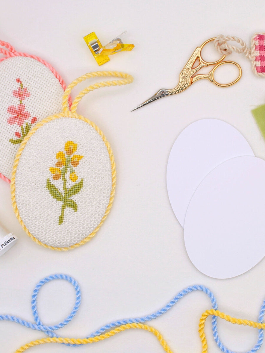 Flower needlepoint ornaments sit atop a table with supplies and tools for self finishing your needlepoint. 