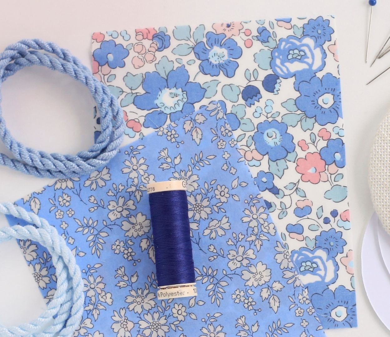 Needlepoint supplies including blue floral finishing fabric, blue finishing thread, and blue cording.