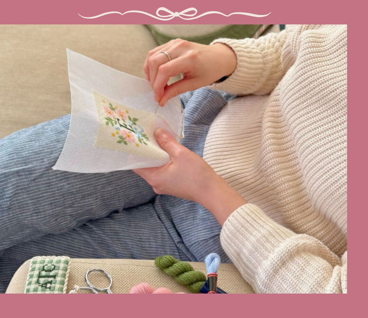 A woman is sitting on a sofa working on a monogrammed needlepoint project.