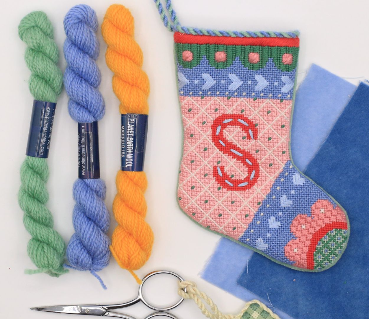 Needlepoint stocking ornament sits next to thread, scissors and velvet finishing fabric.