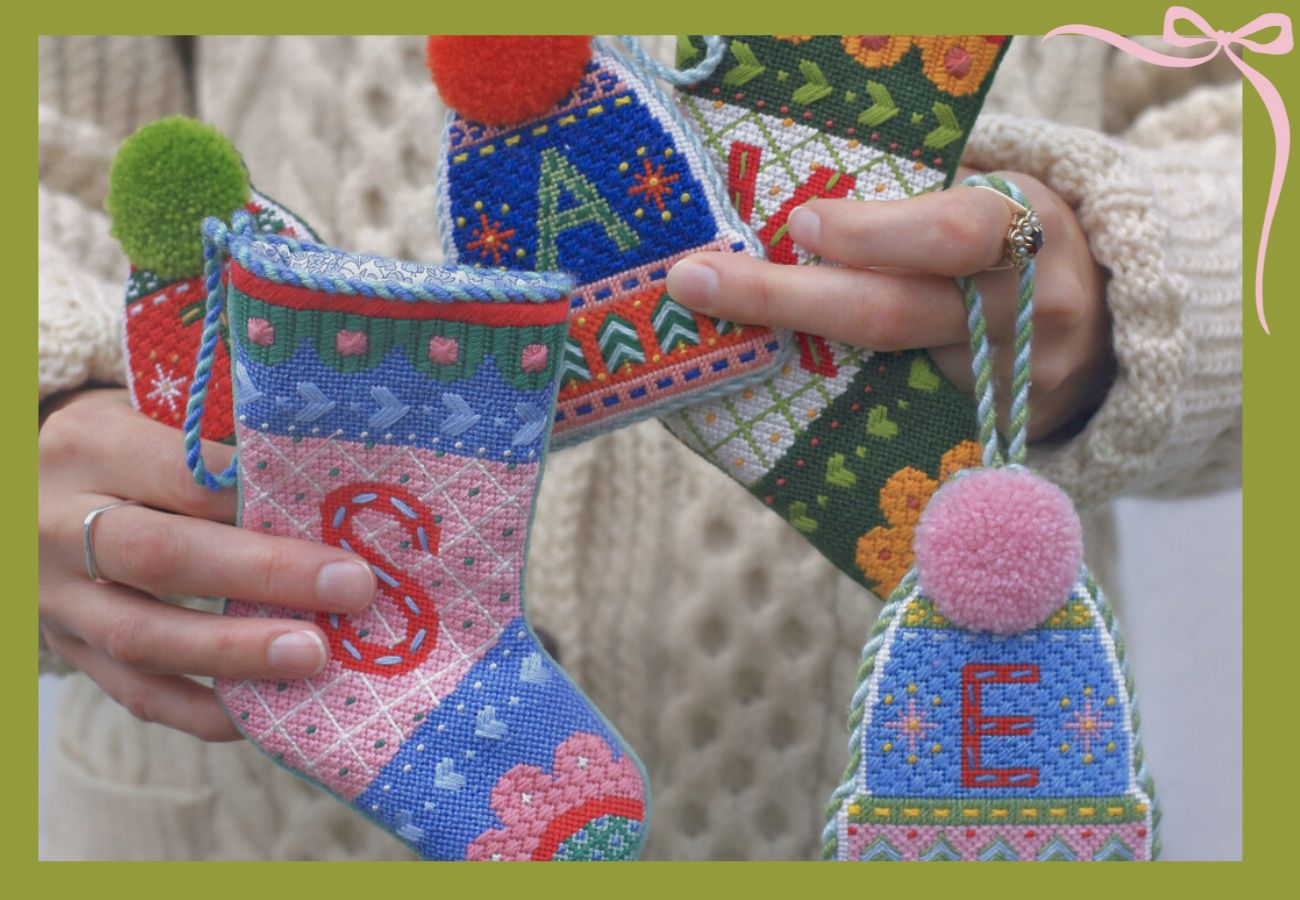 A woman is holding several monogrammed needlepoint holiday ornaments.