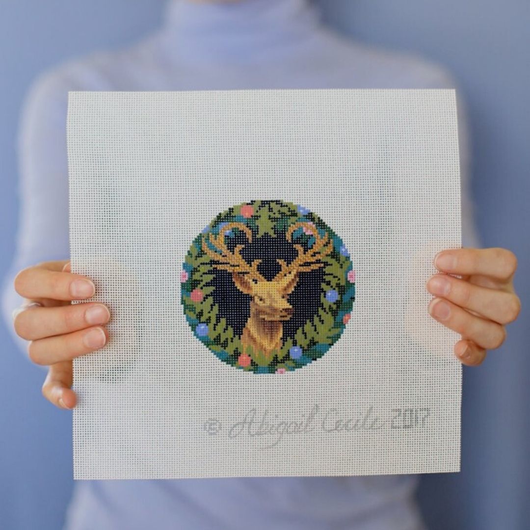 Abby is holding up a completed reindeer needlepoint project.