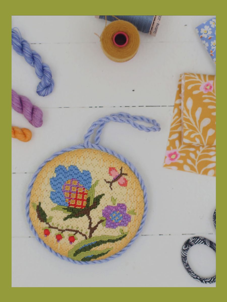 A flower needlepoint ornament sits atop a craft table.