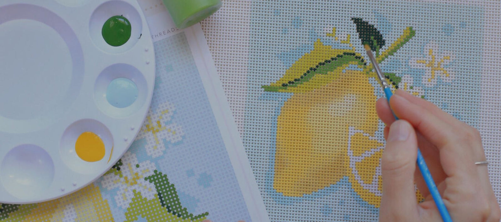 Woman is painting a lemon on needlepoint canvas.
