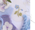 Blue wildflower needlepoint project with completed stitching, on a tabletop surrounded by fresh flowers, finishing fabric, thread, and cording.